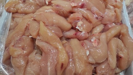 Close-up of fresh raw chicken fillet pieces displayed at a market or store, showcasing uncooked poultry meat with natural texture, color, and detail for food industry use