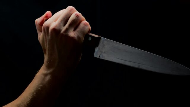 A trembling hand due to the release of darenalin into the blood with a large table knife wants to kill someone on a black background. A frightened criminal swings a sharp knife with a large blade