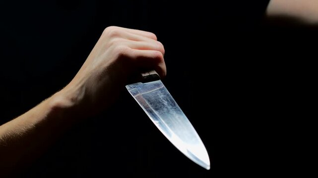 A trembling hand due to the release of darenalin into the blood with a large table knife wants to kill someone on a black background. A frightened criminal swings a sharp knife with a large blade