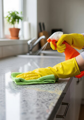 Person with cleaning liquid splash stream from spray bottle landing onto modern kitchen countertop, microfiber cloth, National Cleaning Week, National Cleanliness Day, House Cleaners Day. Vertical