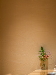 A minimalist interior featuring a textured beige wall and a small decorative vase with colorful flowers, creating a serene ambiance in traditional restaurant for fine dining