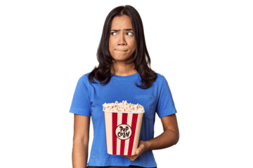 Young woman with popcorn bucket in studio confused, feels doubtful and unsure.