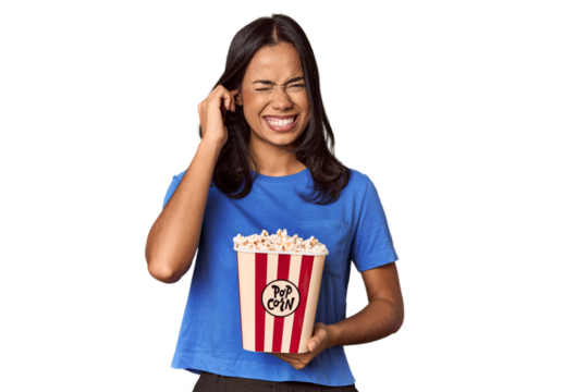 Young woman with popcorn bucket in studio covering ears with hands.