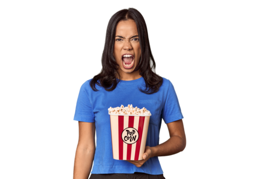 Young woman with popcorn bucket in studio screaming very angry and aggressive.