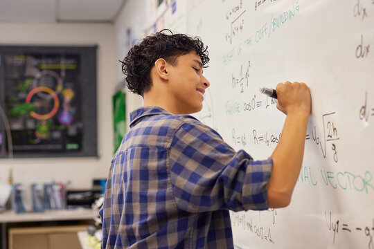 Teen student writing equation on whiteboard in classroom