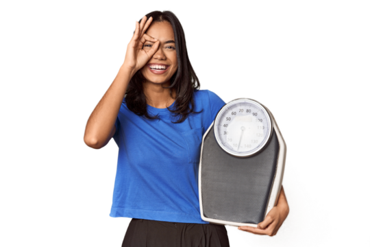 Filipino woman with scale in studio excited keeping ok gesture on eye.