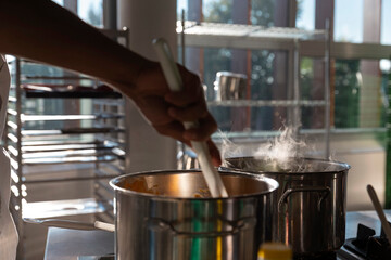 Chef stirring steaming pot in professional kitchen with wooden spoon