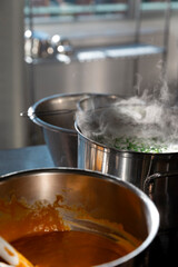 Multiple steaming pots on commercial stove with chef cooking in background