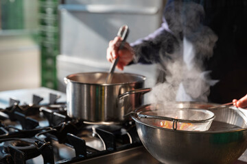 Professional chef managing multiple cooking pots with steaming vegetables in kitchen