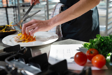 Chef using tongs to place delicate garnish on finished gourmet dish