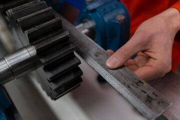 Hand measuring metal gear component with ruler for quality control inspection