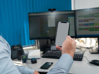 Professional holding smartphone in contemporary office workspace with multiple monitors