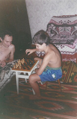 Father and ten-year-old son playing chess in home room during summer vacation, captured in film photography style from early 1990s in Ukraine