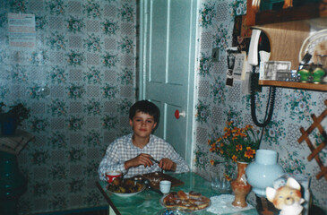 Boy eats at kitchen table, captured in analog photography style from 1990s in Ukraine.