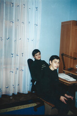 Two teenagers sitting at a table with an old desktop computer in a Ukrainian home room, early 2000s...