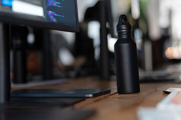 Black water bottle on desk beside computer screen showing programming code