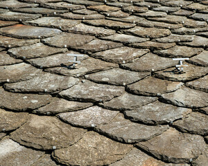A close-up view of a traditional rooftop covered in overlapping, weathered slate shingles, creating a beautiful and intricate texture.