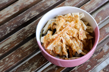 high angle photo from a close distance of a bowl of wonton skin or flour chips sprinkled with peanut sauce arranged on a wooden chair