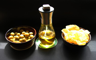 Aceite de oliva virgen extra con brillo dorado oro y amarillo, aceitunas y patatas fritas de aperitivo y tapa sobre fondo negro
