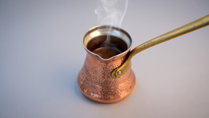 A steaming cezve with a golden handle on a light background creating a warm and inviting atmosphere
