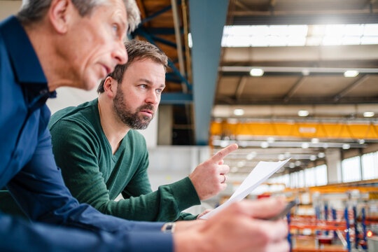 Manager pointing by businessman leaning on railing at factory