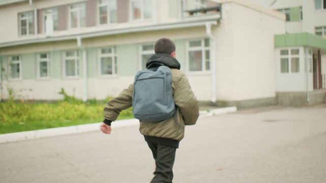 boy with backpack running toward school building glancing sideways under cloudy sky showing determination and energy in motion surrounded by urban residential architecture and greenery