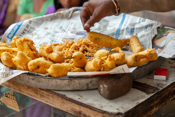 A vendor's hand picks up a freshly fried savory snack, likely a pakora or bhaji, from a street food stall. This image captures a moment of authentic street food culture, perfect for design projects re
