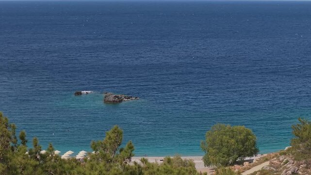Aerial drone shot revealing Achata Beach in Karpathos, Greece, with pine trees framing the coastline