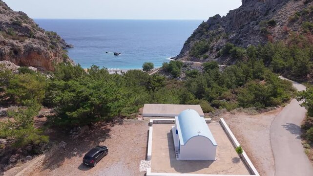 Aerial drone ascending behind a chapel to reveal Achata Beach and the surrounding seascape in Karpathos, Greece