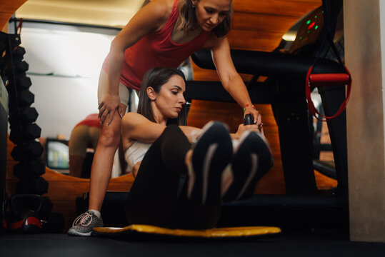 Determined sportswoman doing crunches with personal trainer assistance