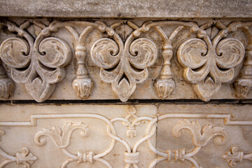 A close-up of weathered marble with intricate bas-relief carvings, featuring detailed floral and geometric patterns. Ideal for architectural history, interior design, and cultural documentation.
