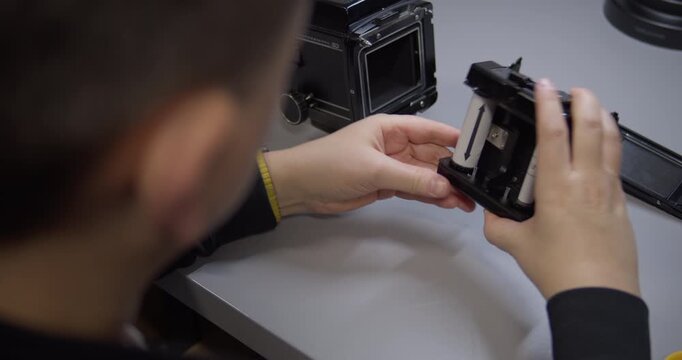 An over-the-shoulder view of a photographer loading 120 film. Their hands carefully place a new roll film spool into the insert of a medium format camera back before shooting.