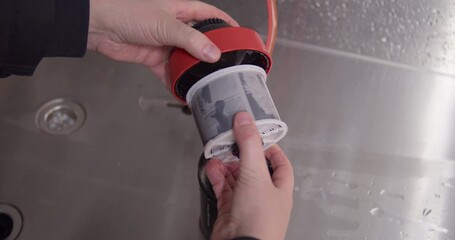 The moment of truth in analog photography. A photographer's hands carefully pull the wet, developed 120 film negative from its developing reel over a darkroom sink.