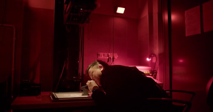 Working under a red safelight, a photographer leans over an enlarger's easel, using a grain focuser to achieve critical sharpness before making a print. The essence of analog craftsmanship.