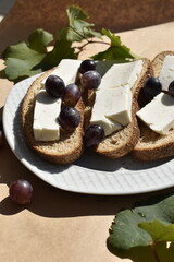 Close-up bread slices with cottage cheese and grapes on plate on parchment paper among grapes and leaves, top view
