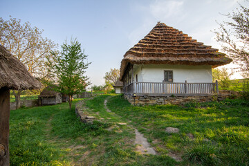 Fototapeta premium A charming, traditional thatched-roof cottage with a white facade and a rustic fence, nestled in a lush green landscape. Perfect for travel blogs, folk art inspiration, and historical preservation con