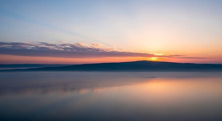 Naklejka premium Sunrise over a misty lake with silhouetted layered hills and sun rays