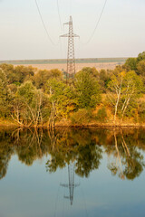 Obraz premium A serene, balanced landscape featuring a power line tower reflected in a calm body of water. The composition perfectly blends industrial elements with the tranquil natural scenery for a modern, reflec