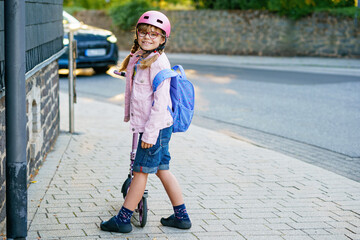 Happy elementary school girl riding a scooter to school wearing a helmet and backpack. Safe,...
