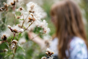 Portrait of happy elementary school girl with glasses playing outdoors in summer meadow, blowing...