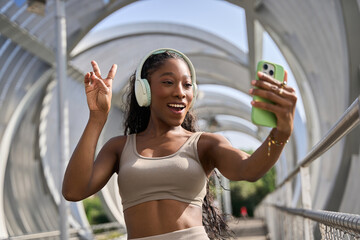 Young sporty woman making video call wearing headphones on modern bridge
