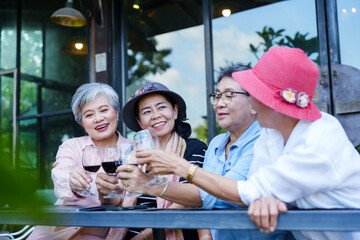 Group of senior Asian women toasting glasses smiling drinking wine outdoor cafe casual clothing...