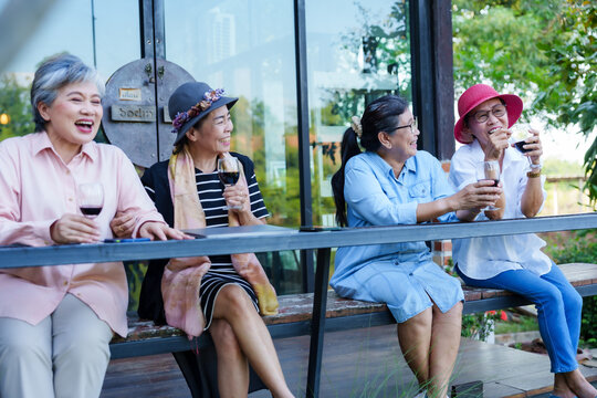 Senior Asian women sitting outdoor cafe drinking wine casual clothing cheerful greenery enjoying lifestyle leisure friendship retirement happiness communication vacation freedom togetherness