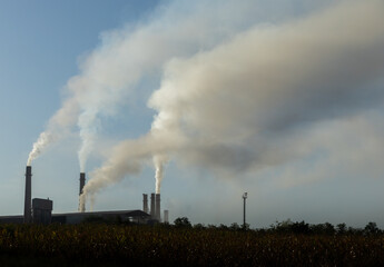 Industrial pollution billowing from factory smokestacks against a blue sky.

