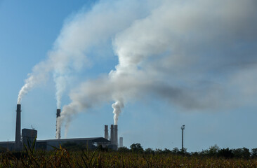 Industrial pollution billowing from factory smokestacks against a blue sky.

