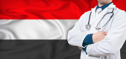 Yemen healthcare concept. Male doctor on Yemen flag. Doctor with crossed arms on Yemen flag