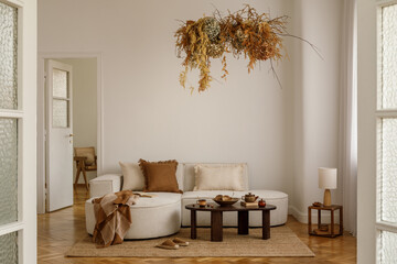 Warm-toned living room with beige sofa, dried floral chandelier, wooden coffee table with rustic...