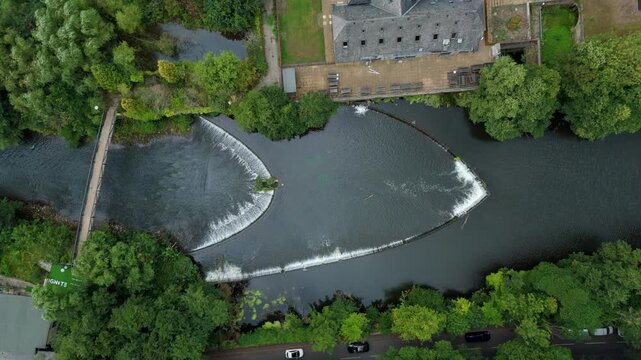 Top down aerial drone view of large bow shaped Weir on river Derwent, water control structure, Millbrook in Derbyshire Dales in England UK