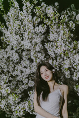 Woman in a delicate white dress standing amidst blooming flowers at night.
