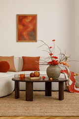 Living room styled with warm orange tones, decorative vase with red flowers, beige sofa and wooden...